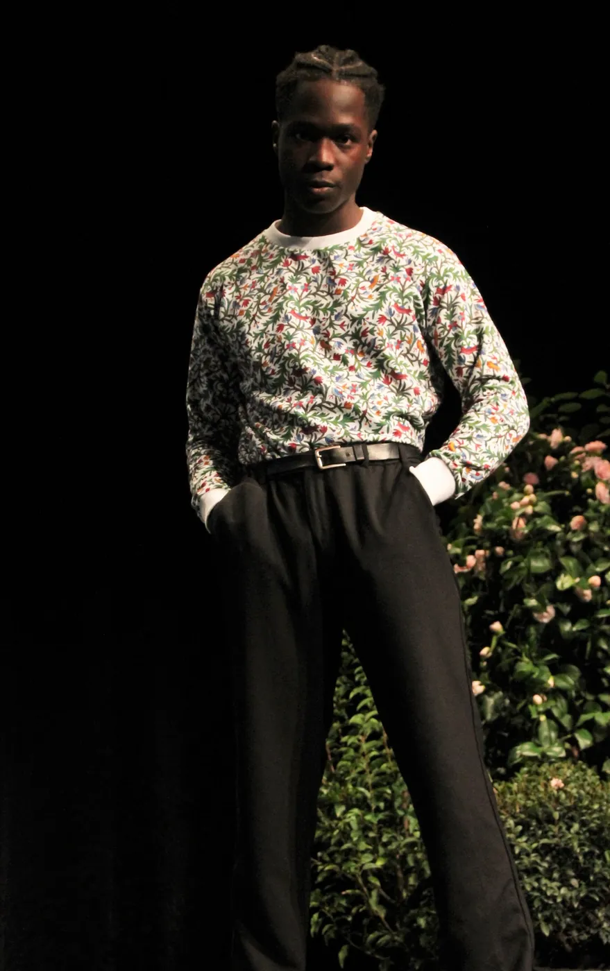 Un mannequin en chemise à petites fleurs et pantalon noir, sur le podium de l'Amphimax
