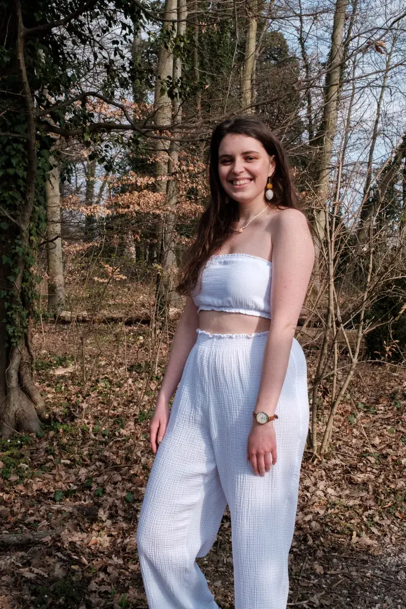 Une mannequin en haut bandeau blanc et pantalon blanc, dans la forêt