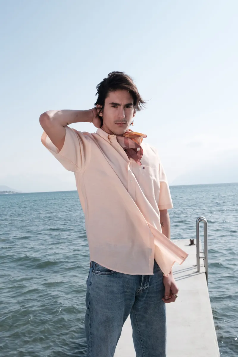 Un mannequin en chemise rose pâle sur un ponton, la main dans les cheveux