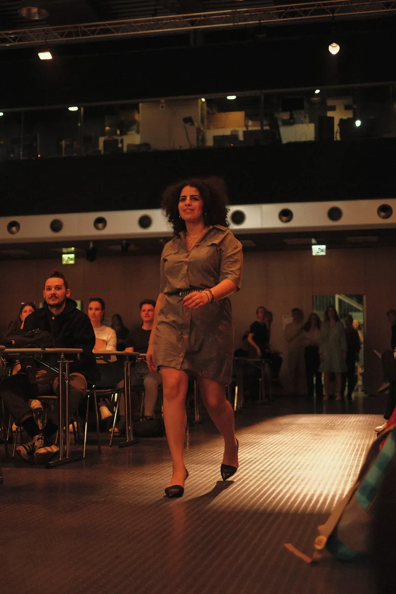 Une mannequin en robe chemise kaki avance sur le podium