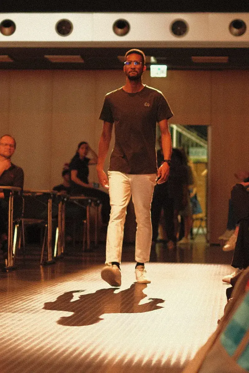 Un mannequin en t-shirt noir et pantalon blanc avance sur le podium
