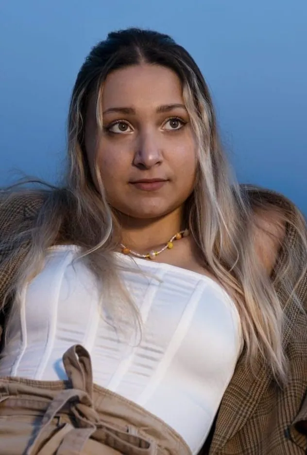Portrait d'une jeune femme qui porte un collier doré, devant un ciel bleu