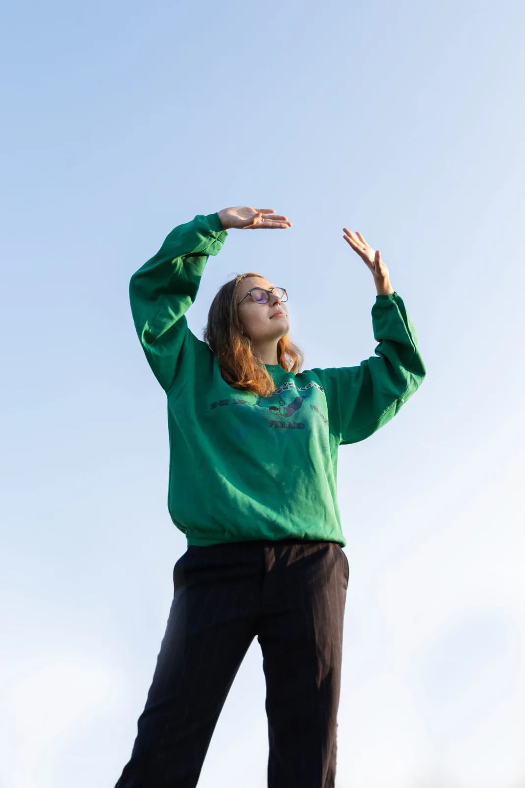 Une mannequin en sweat vert, les bras levés devant le ciel