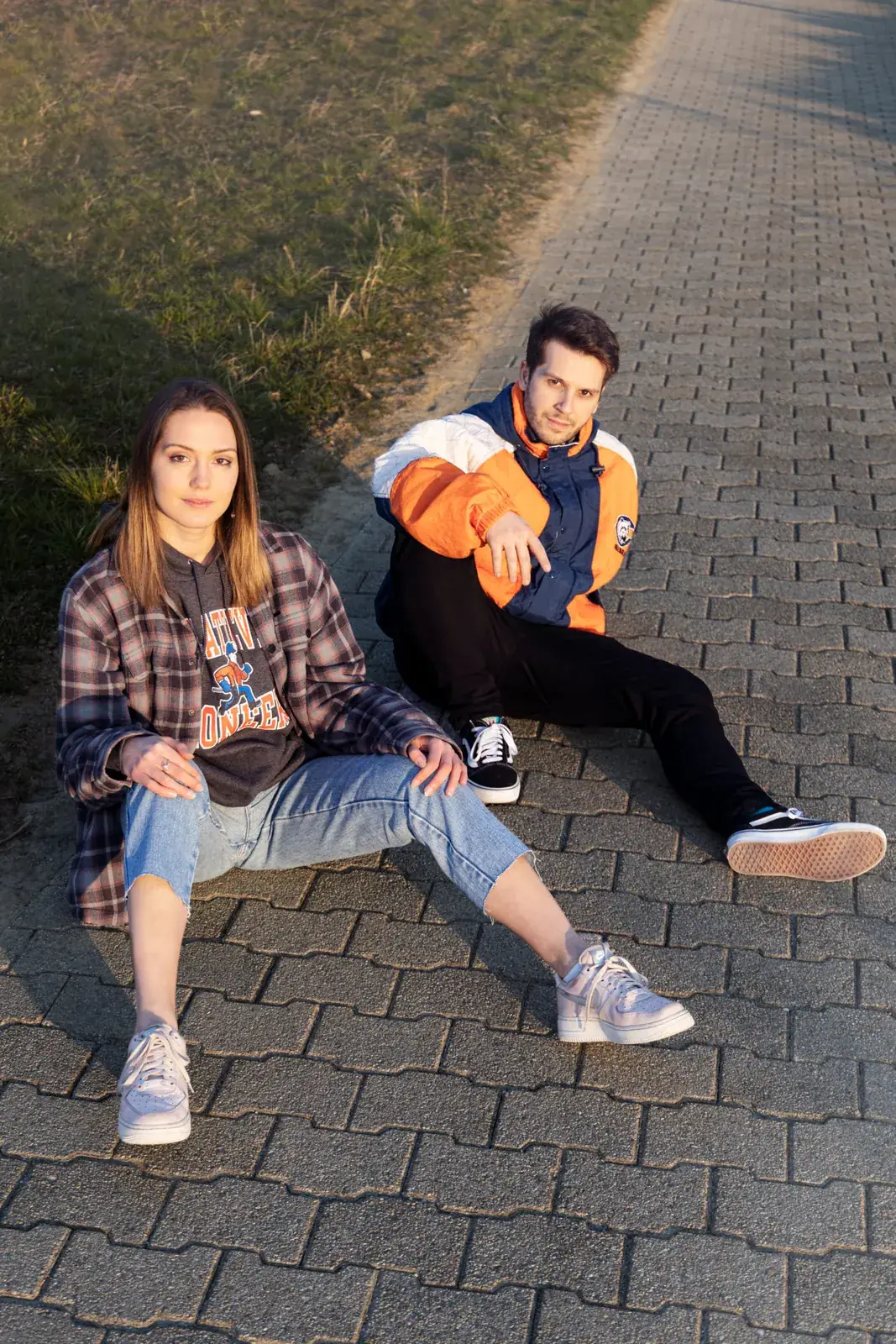 Deux mannequins assis sur des pavés, en chemise à carreaux et veste orange