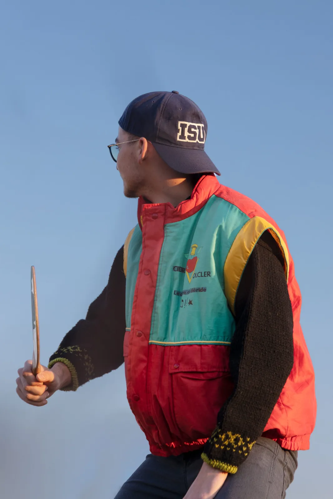 Un étudiant en veste vintage rouge, verte et jaune et en casquette, photographié devant un ciel bleu