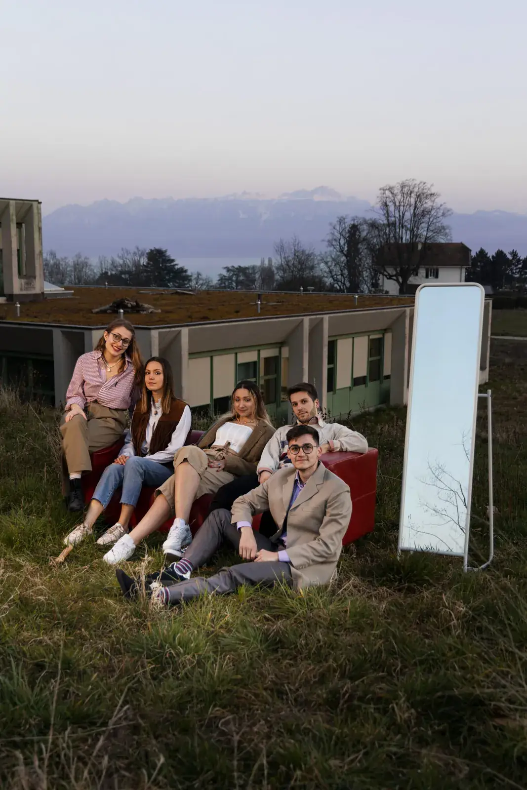 Les mannequins sur un canapé dans l'herbe, à côté d'un miroir, avec le lac et les Alpes au fond