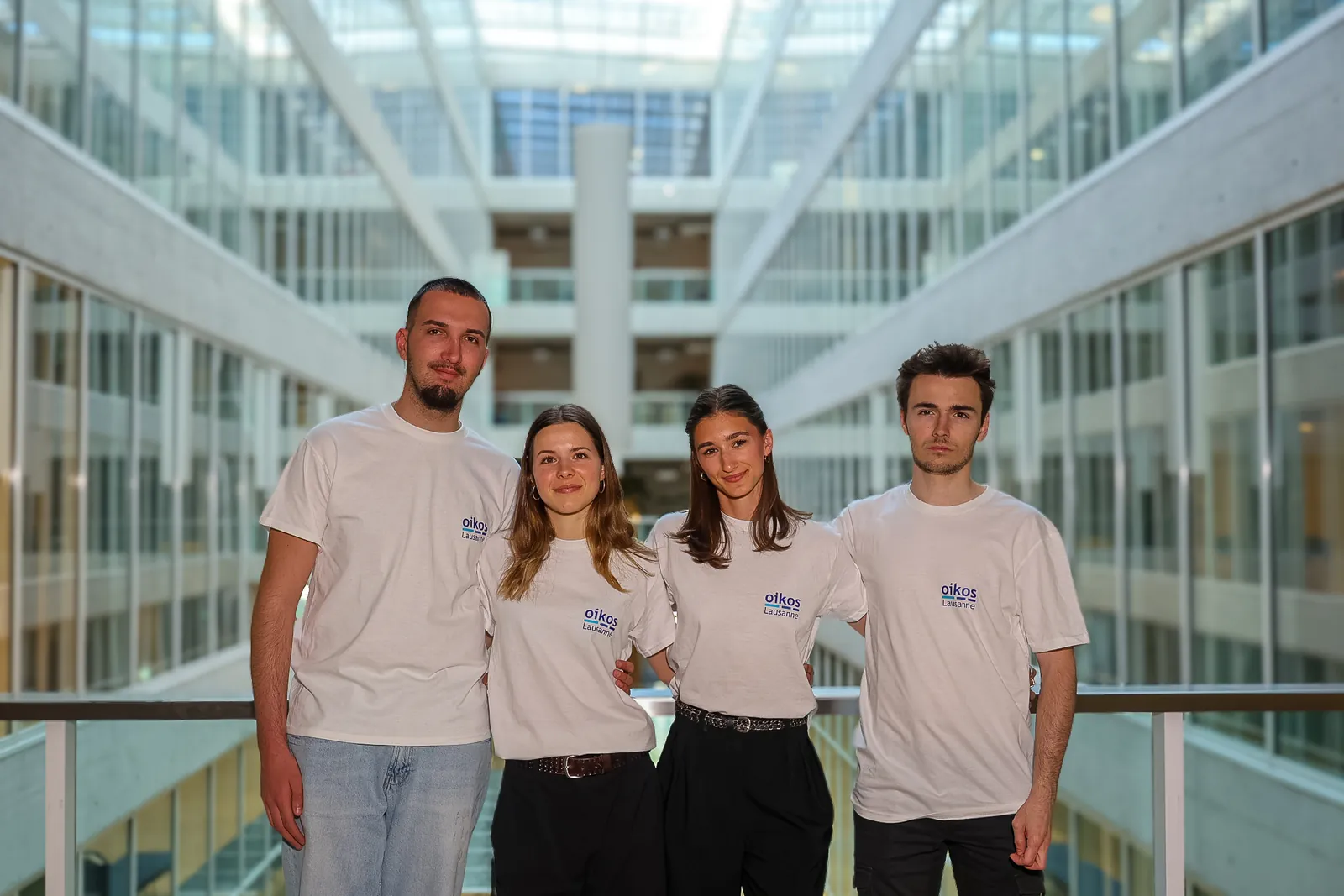 Quatre membres du département Finance en t-shirt oikos, sur une passerelle du campus