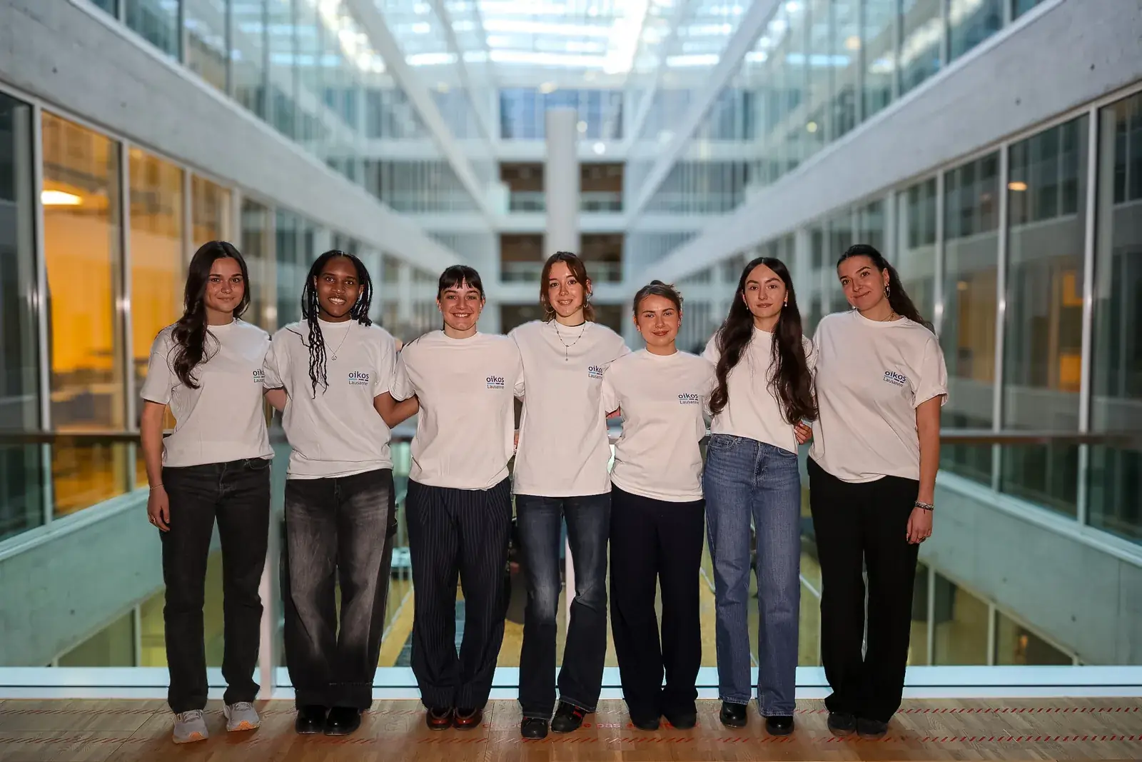 Sept membres du département Marketing en t-shirt oikos, alignées sur une passerelle du campus